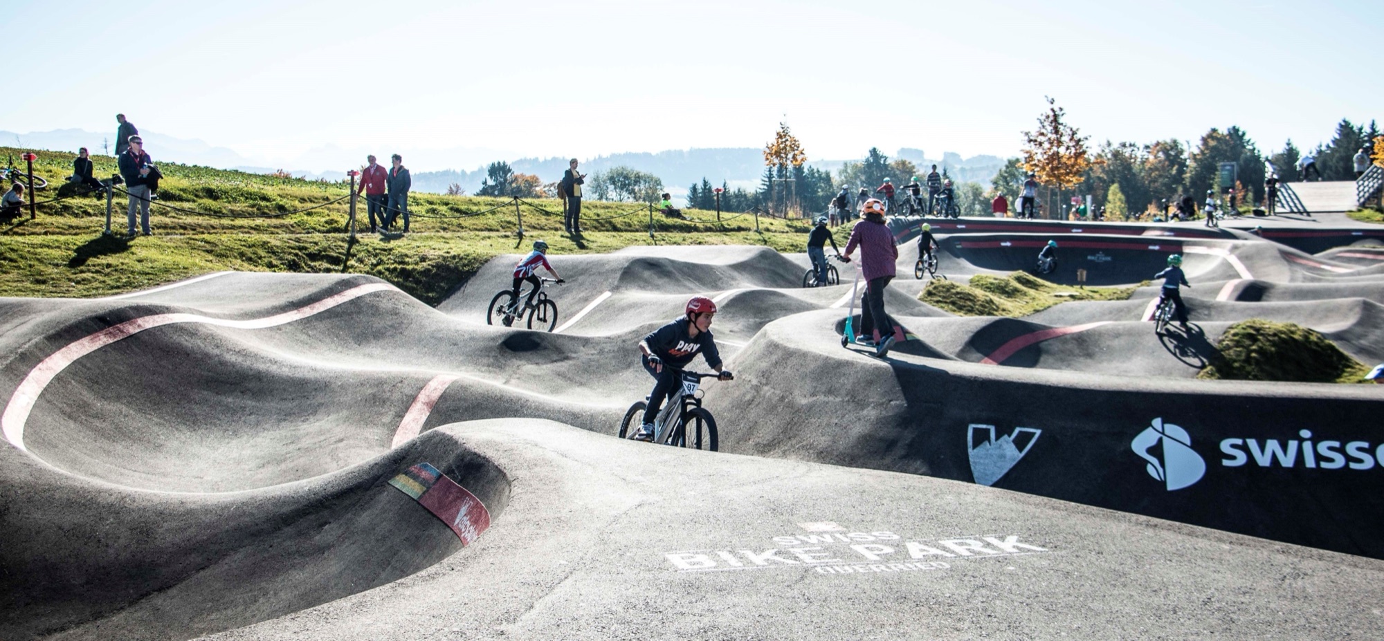 Kinder fahren auf dem Pumptrack des Swiss Bike Park vor Alpenpanorama